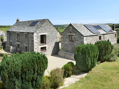 Two stone buildings with solar panels on the roofs surrounded by bushes and grassy land at Westhayes in Camelford