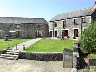A stone built house and outbuilding with a gravel path grass yard and outdoor tables with umbrellas at Westhayes Camelford