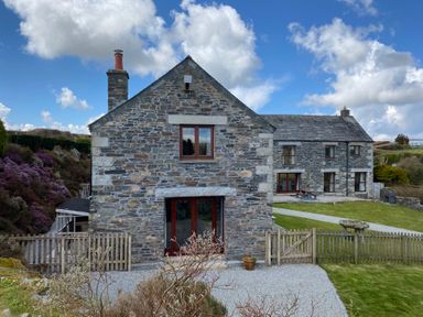 A stone house with wooden windows and a chimney surrounded by a garden with grass and a wooden fence at Westhayes in Camelford