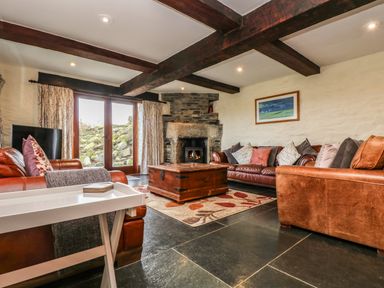 A living room with leather sofas a stone fireplace wooden coffee table and glass doors at Westhayes in Camelford