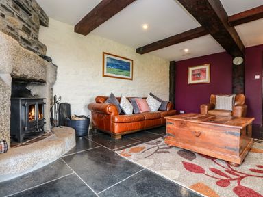 A living room with a brown leather sofa a wooden coffee table a stone fireplace and exposed wooden beams at Westhayes in Camelford