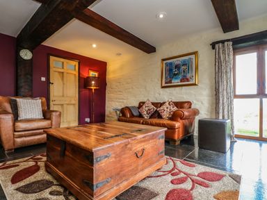 A living room with leather sofa and armchair wooden coffee table and colorful rug at Westhayes in Camelford