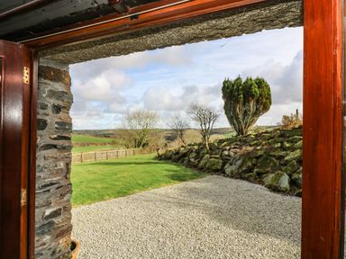 A garden with gravel path grass lawn stone wall and trees viewed through a doorway at Westhayes in Camelford