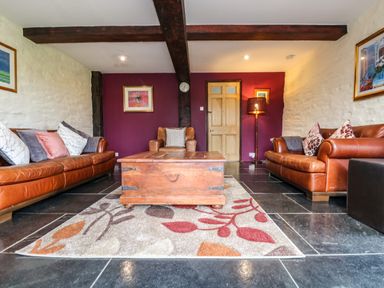 A living room with two brown leather sofas, an armchair, a wooden coffee table on a patterned rug and exposed wooden beams at Westhayes in Camelford