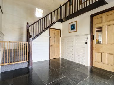 A hallway with dark stone tile floor wooden stairs with a baby gate wooden doors and a framed picture on the wall at Westhayes in Camelford