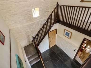 A staircase with carpeted steps and wooden railings leading to a landing with dark stone tile flooring and a wooden door at Westhayes Camelford
