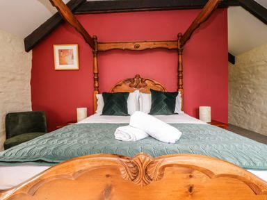 A bedroom with a wooden four poster bed green pillows and white rolled towels on the bed at Westhayes in Camelford