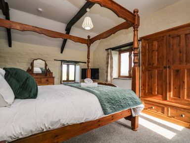 A bedroom with a wooden four-poster bed dresser wardrobe and windows at Westhayes in Camelford