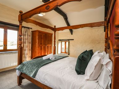 A bedroom with a wooden four-poster bed green pillows and blanket wooden wardrobe and windows at Westhayes in Camelford