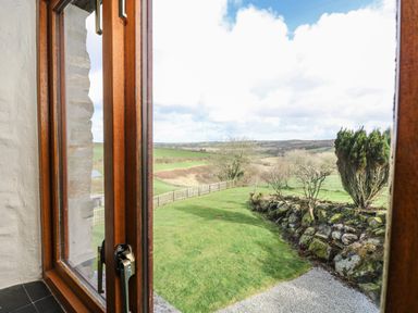 A view of a garden with grass a stone wall and trees seen through a wooden window frame at Westhayes in Camelford