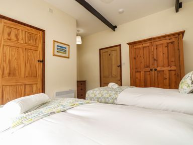 A bedroom with two single beds wooden doors a wooden wardrobe and a chest of drawers at Westhayes in Camelford