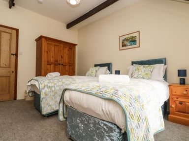 A bedroom with two single beds with patterned throws a wooden wardrobe and bedside table with lamps at Westhayes in Camelford