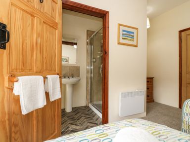 A bedroom view showing an open wooden door leading to a bathroom with a pedestal sink and glass shower at Westhayes in Camelford
