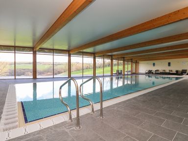 An indoor swimming pool with large windows showing a green landscape at Westhayes in Camelford
