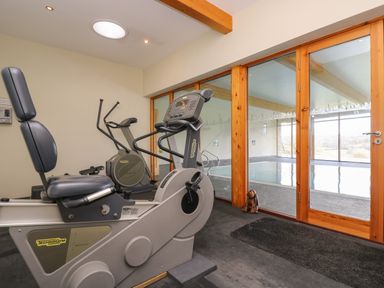 A gym room with exercise bikes and a glass door leading to an indoor swimming pool at Westhayes in Camelford