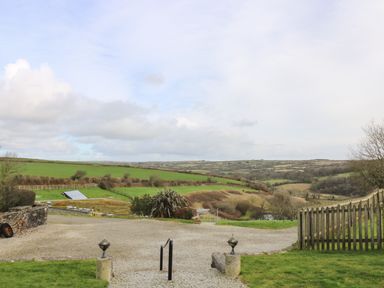 A rural landscape with green fields, a gravel driveway, wooden fence, and distant hills at Westhayes in Camelford