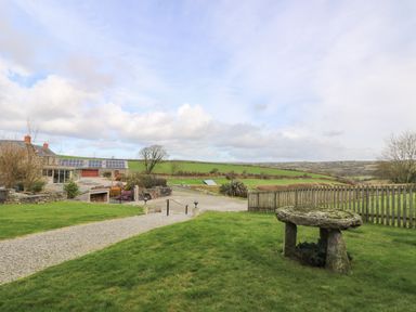 A gravel driveway leads to a house with solar panels on the roof surrounded by green fields and a stone table on a lawn at Westhayes in Camelford