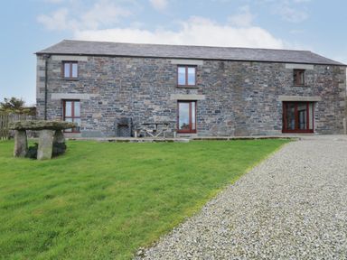 A stone building with a gravel path and green lawn with a stone table and wooden benches at Westhayes in Camelford