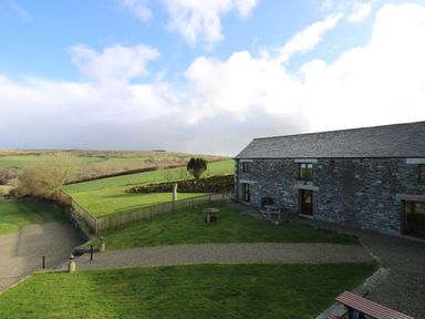 A stone building with a slate roof next to green grass and a gravel pathway at Westhayes in Camelford