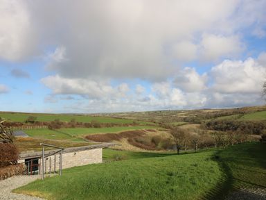 A landscape view of green fields trees and a house with a flat roof at Westhayes in Camelford