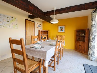 A dining room with wooden chairs around a table set with plates and bowls and a yellow wall with cabinets at Westhayes in Camelford