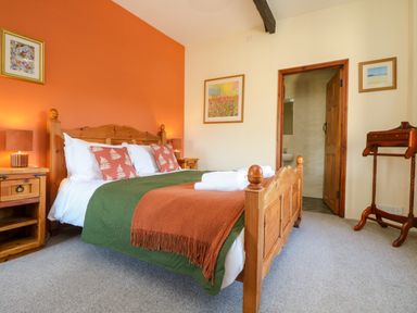 A bedroom with wooden bed frame green and orange bedding bedside tables with lamps and framed pictures on walls at Westhayes Camelford