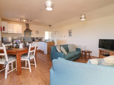 An open plan room with a kitchen area a wooden dining table with chairs and a seating area with sofas and a television at Kerensa ha-Kres in Sennen