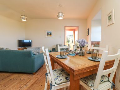 A dining table with four chairs and a vase of flowers in a living room with sofas and a television at Kerensa ha-Kres in Sennen