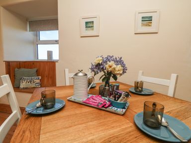 A dining table set with blue plates and transparent cups with spoons a white teapot a tray with tea packets and a vase with flowers in a dining area at Kerensa ha-Kres in Sennen