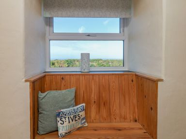 A window seat with wooden paneling cushions and a lamp on the windowsill at Kerensa ha-Kres in Sennen