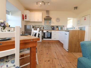 A kitchen with a wooden dining table and white chairs near appliances and blue tiled backsplash at Kerensa ha-Kres in Sennen
