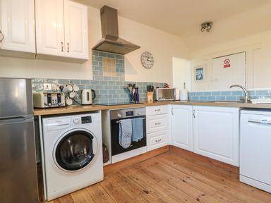 A kitchen with white cabinets blue tiled backsplash wooden countertops and wooden floor at Kerensa ha-Kres in Sennen