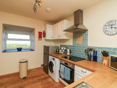 A kitchen with wooden floors white cabinets blue tiled backsplash and appliances at Kerensa ha-Kres in Sennen