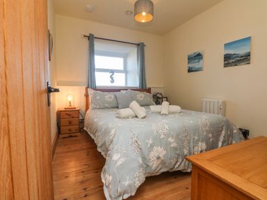 A bedroom with a double bed floral bedding bedside table lamp wooden furniture and paintings on the wall at Kerensa ha-Kres in Sennen