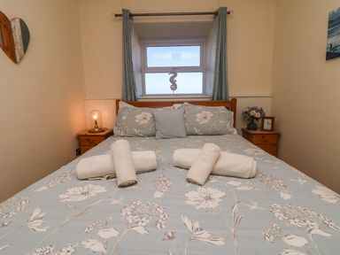 A double bed with floral bedding and rolled towels with bedside tables and a window at Kerensa ha-Kres in Sennen