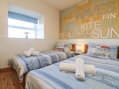 A bedroom with two single beds blue striped bedding white rolled towels and a window with a blue blind at Kerensa ha-Kres in Sennen