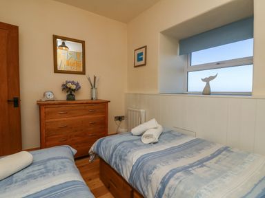 A bedroom with two single beds a wooden chest of drawers and a window with a whale tail ornament at Kerensa ha-Kres in Sennen