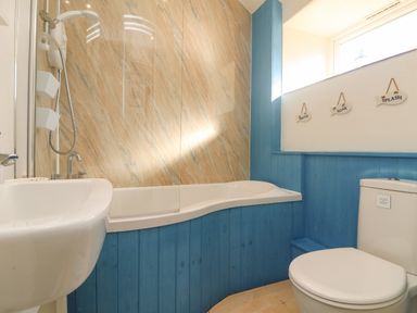 A bathroom with a white bathtub and shower next to a toilet and sink with blue wooden paneling at Kerensa ha-Kres in Sennen