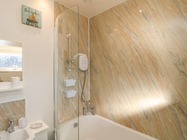 A bathroom with a bathtub shower combination white fixtures and beige marble patterned walls at Kerensa ha-Kres in Sennen