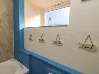 A bathroom wall with four fish-shaped signs hanging under a frosted window at Kerensa ha-Kres in Sennen