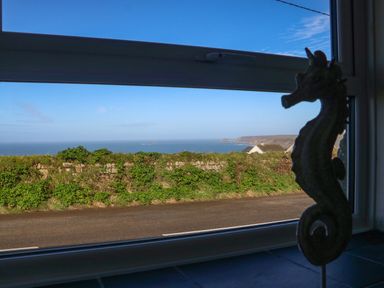 A view of a coastal road with greenery and the sea in the distance seen through a window with a seahorse decoration at Kerensa ha-Kres in Sennen