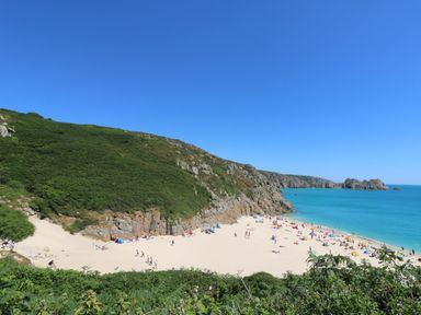A sandy beach with people sunbathing and swimming near cliffs and green vegetation at Kerensa ha-Kres in Sennen