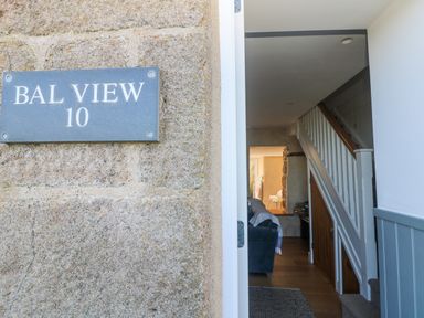 An entrance door open to a hallway with stairs and a living area at Bal View in St Just