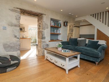 A living room with a blue velvet sofa a wooden coffee table and exposed stone walls at Bal View in St Just