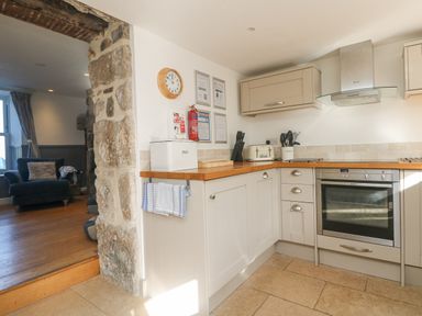 A kitchen with wooden countertops a wall oven and a stone wall near an opening to a living room at Bal View in St Just
