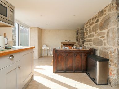 A kitchen with wooden countertop a dark wooden table stone wall and a metal trash bin at Bal View in St Just