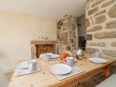 A dining table set with plates mugs croissants and a teapot in a room with stone walls and a fireplace at Bal View in St Just