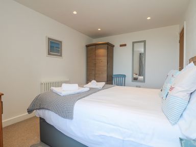 A bedroom with a bed with pillows and folded towels a wooden wardrobe a blue chair a wall mirror and a framed picture at Bal View in St Just