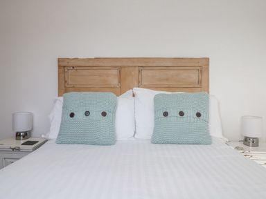 A bed with wooden headboard white pillows blue knitted cushions and bedside tables with lamps at Bal View in St Just