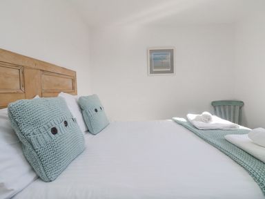 A bedroom with a wooden headboard two knitted pillows white bed linens a green chair and towels at Bal View in St Just